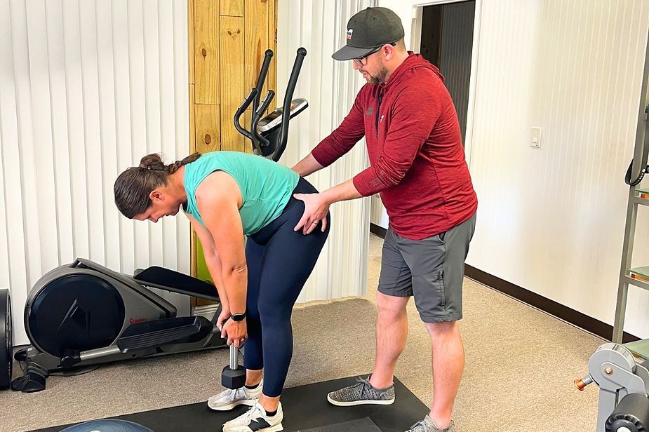 A man is helping a woman lift a dumbbell in a gym.
