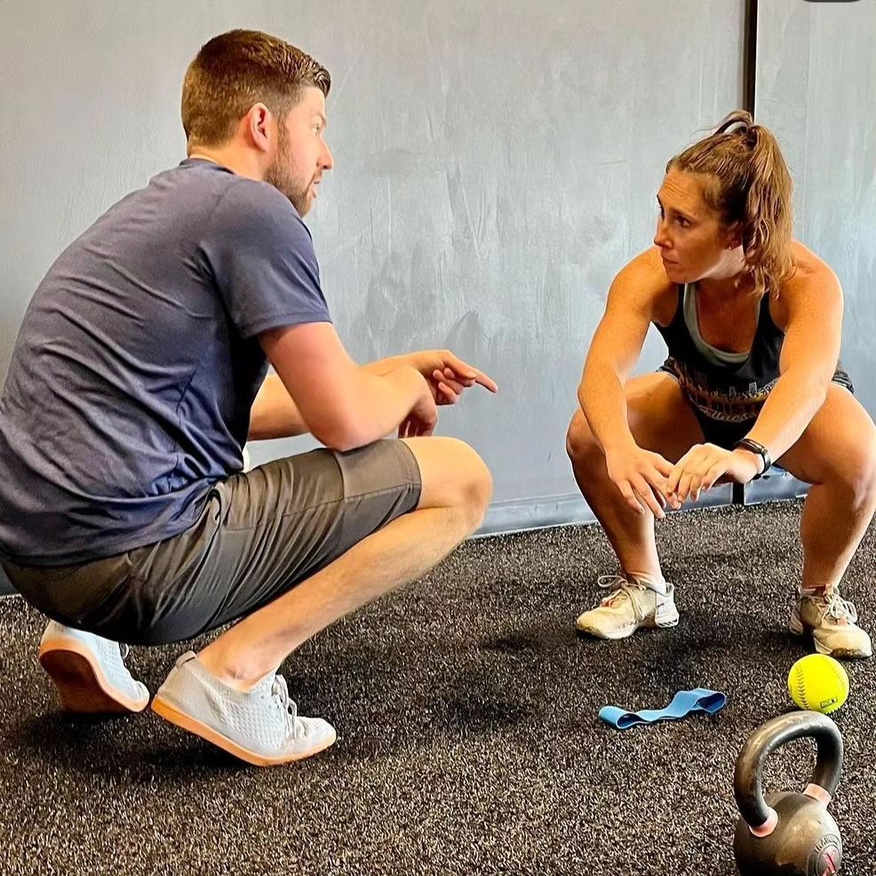 A man is helping a woman do exercises on a bench in a gym.