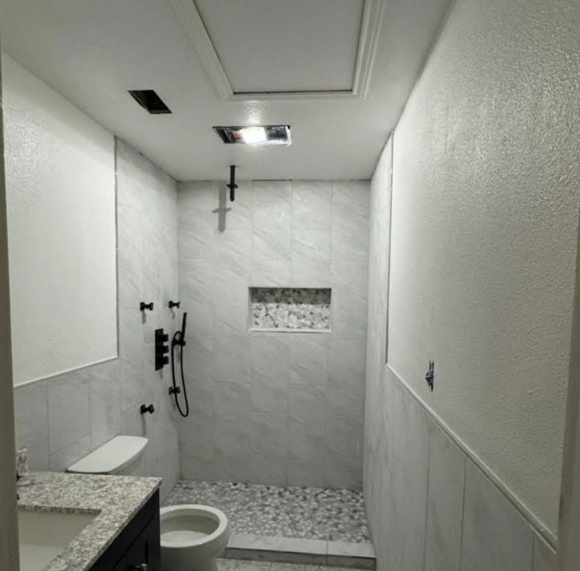 Bathroom with gray tile shower, toilet, black fixtures, and white walls.
