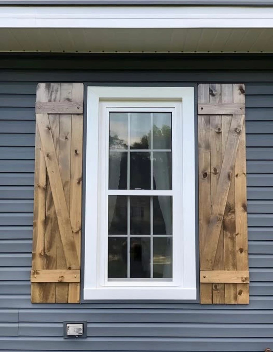 Window with white frame, surrounded by gray siding and wooden, rustic shutters.