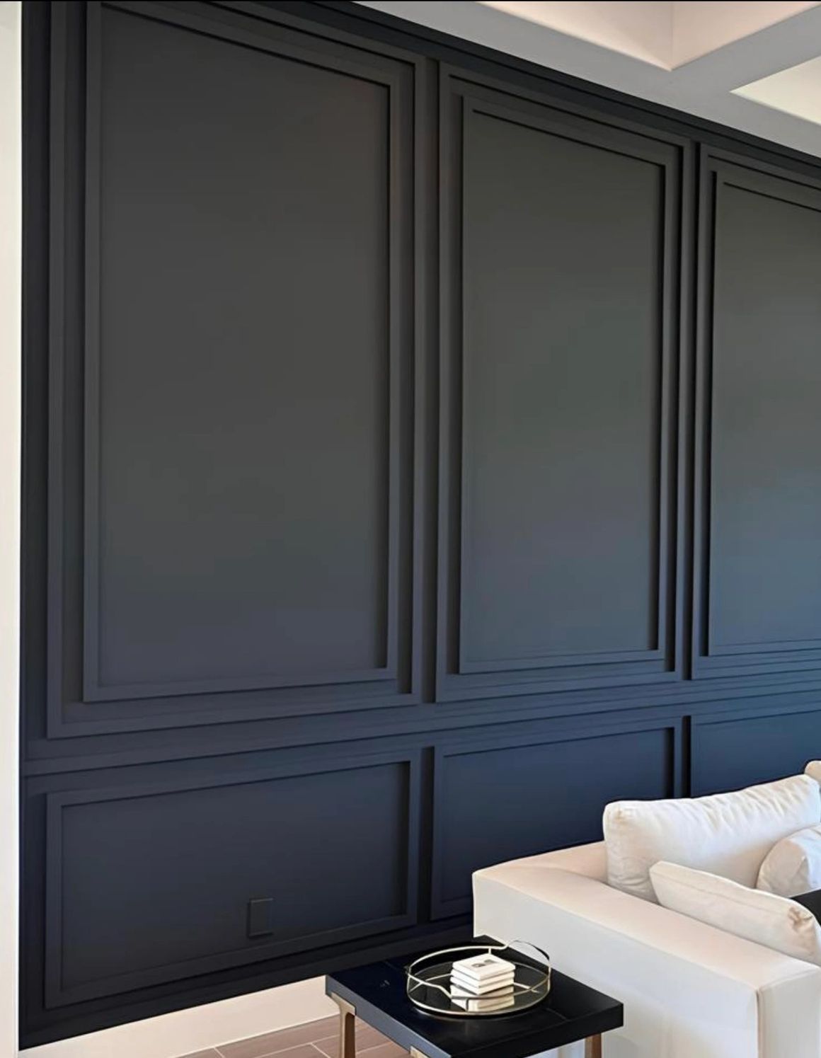 Black paneled wall with decorative molding, framing a white couch and side table.