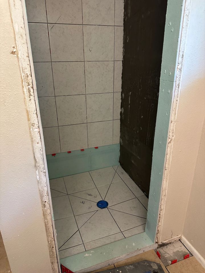 Shower stall with tile floor and walls, blue drain, and green waterproofing.