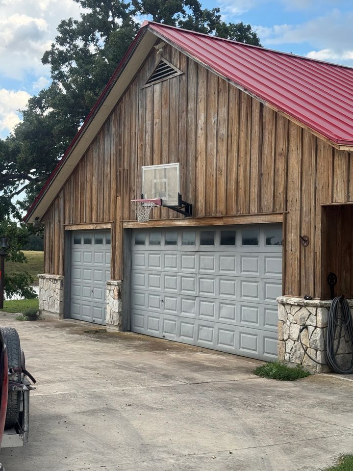 Two-car garage with wooden siding, gray doors, red roof, and basketball hoop; set outdoors.