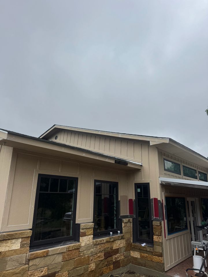 Beige building with black-framed windows, stone base, under overcast sky.