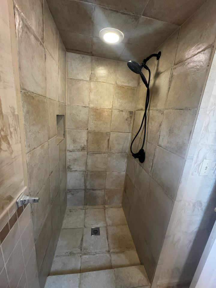 Tiled shower with a handheld showerhead, recessed shelf, and overhead light.