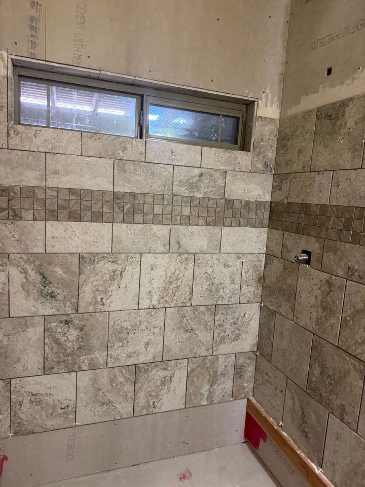 Bathroom wall under construction with beige and brown tiles, small window, and unfinished base.