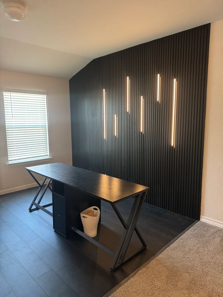 Modern home office with black wood desk, accent wall with vertical lines, and linear lights.