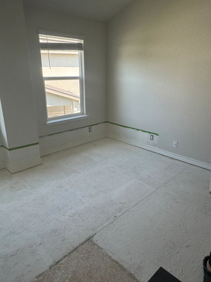 Empty room with window, light carpet, and painter's tape along the walls.