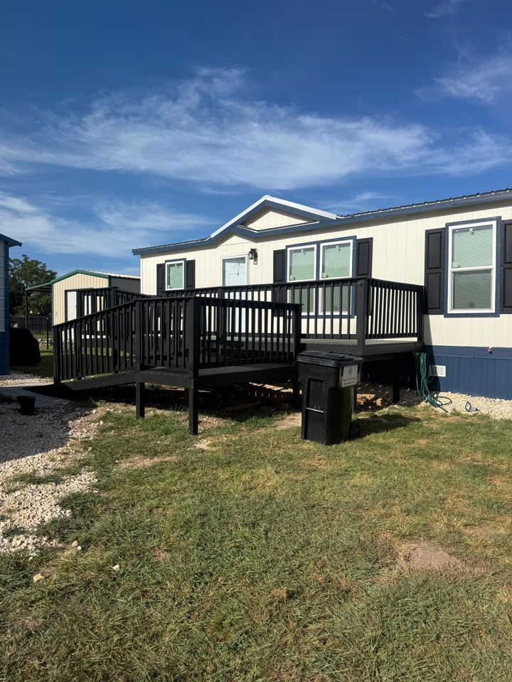 Mobile home with a black ramp, deck, and dark blue accents on a bright day.
