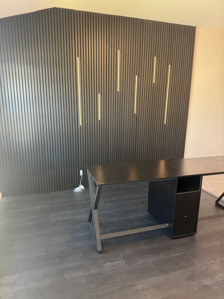 Black desk in front of a black ribbed accent wall with vertical gold lights.