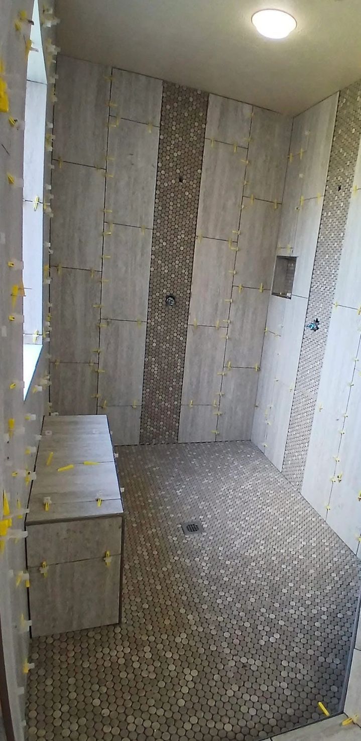 Shower under construction with gray and pebble tile design. Bench included.