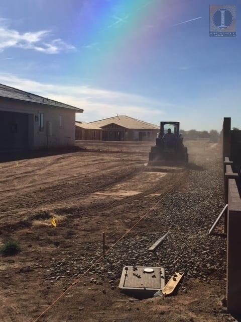 A bulldozer is working on a dirt road with a rainbow in the background.