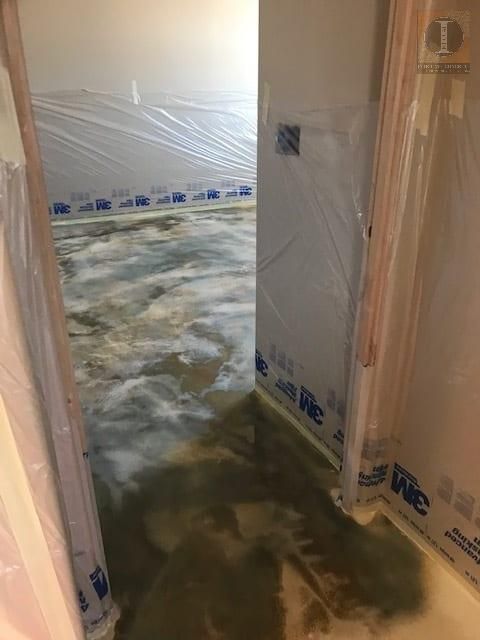 A room with a flooded floor and a door covered in plastic.