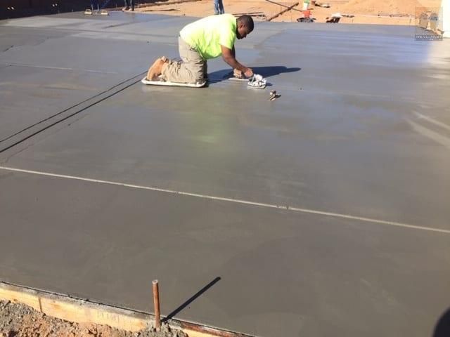 A man is kneeling on the ground spreading concrete