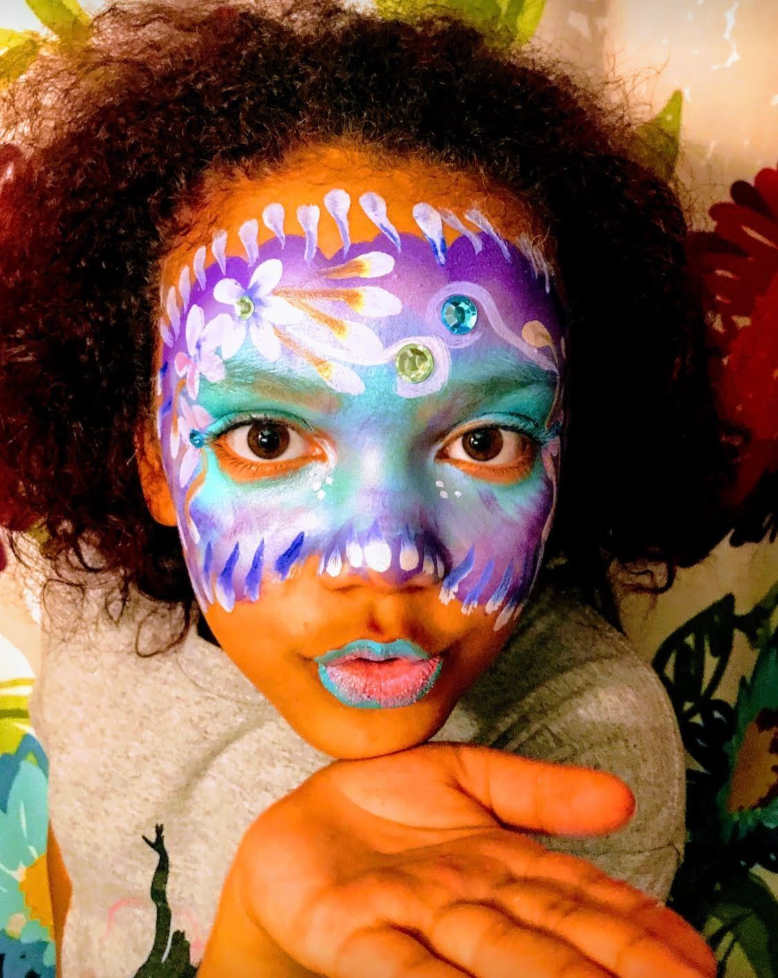 Kids Face Painting Child with colorful floral face paint, holding out an open hand toward the camera.