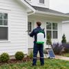 Person spraying a white house with a backpack sprayer. Solar panel on the ground.