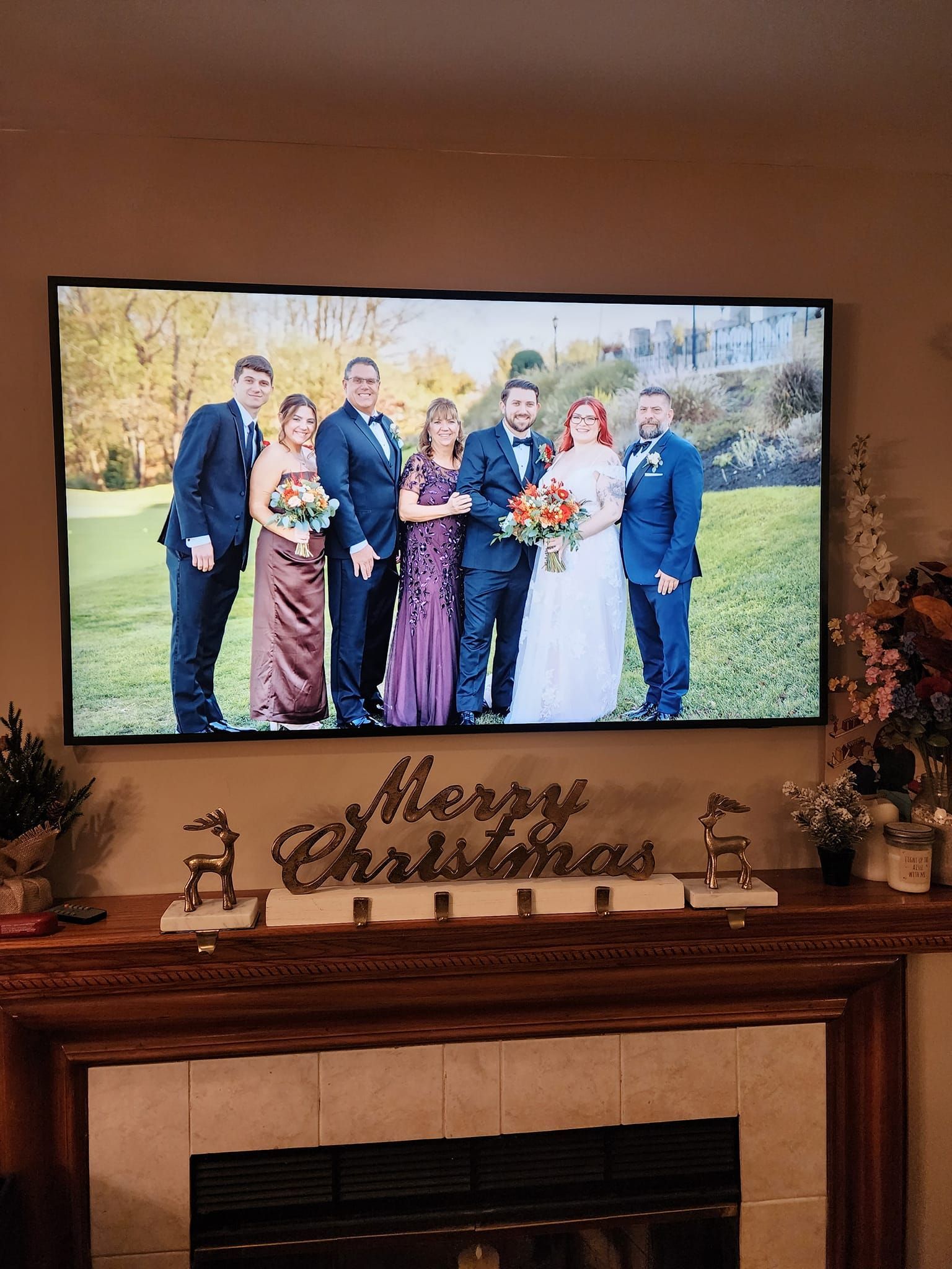 Wedding photo on TV above a fireplace mantel decorated for Christmas.