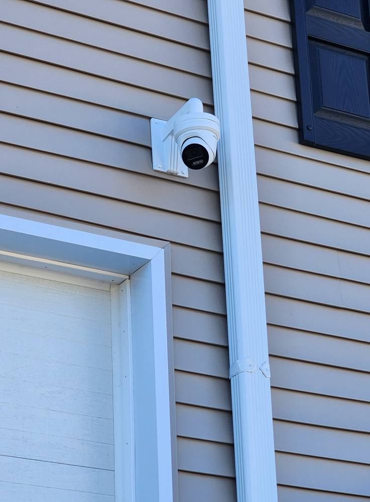 Security camera mounted on a building's siding near a downspout and door frame.