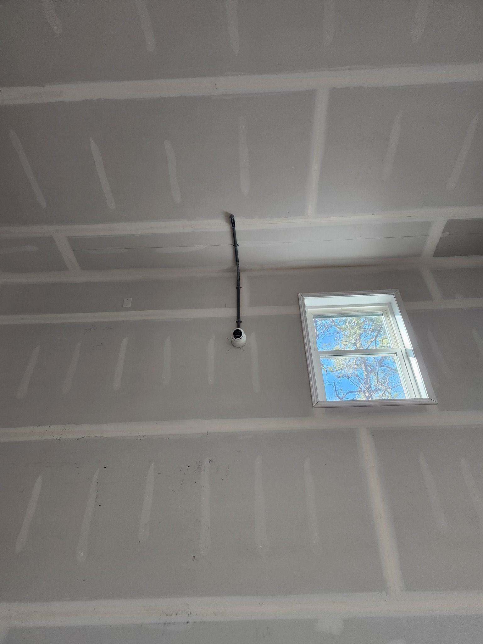 Drywall and unfinished ceiling with exposed wiring, and a small window.