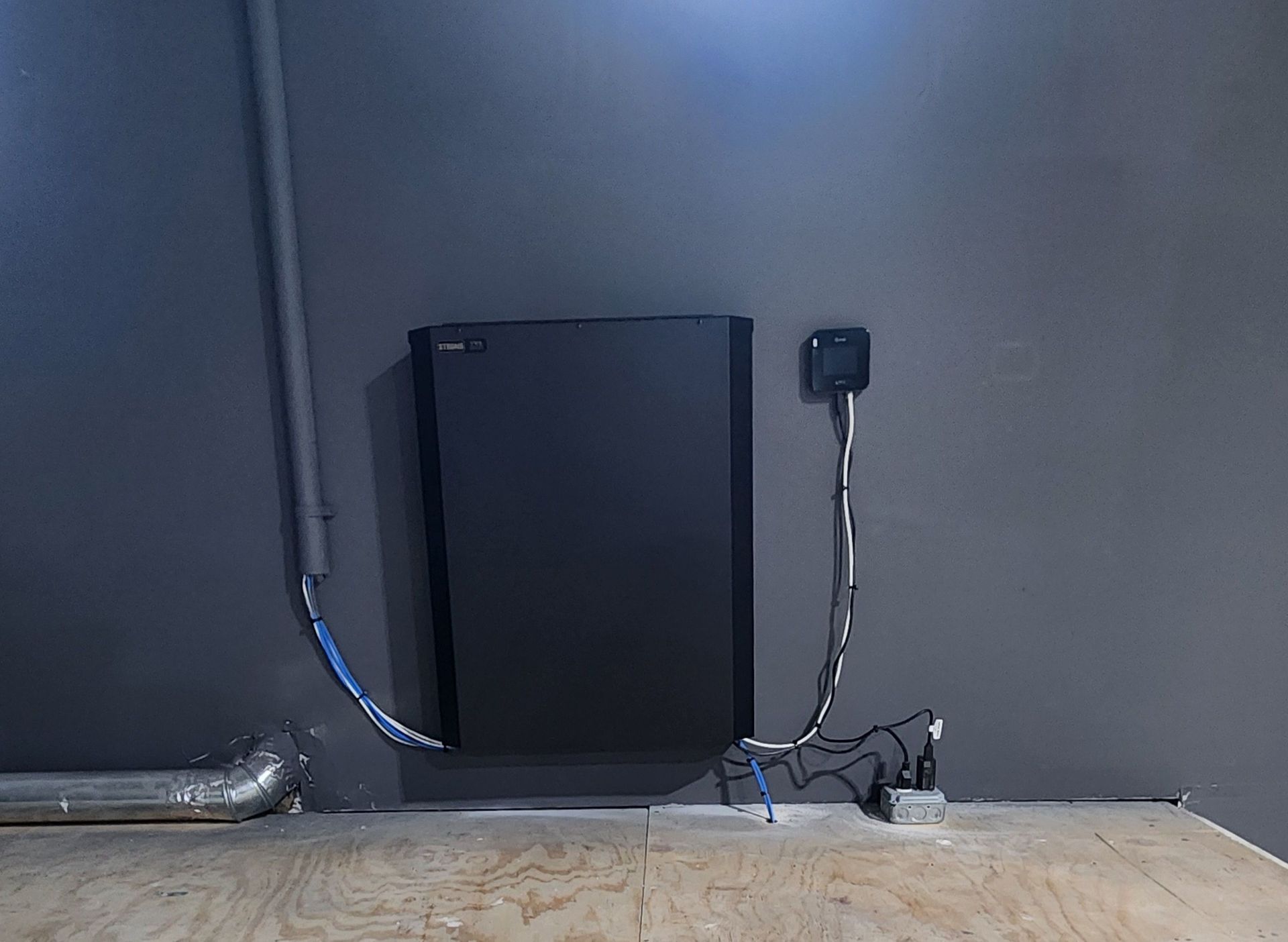 Black electrical panel mounted on a gray wall with conduit and wiring.