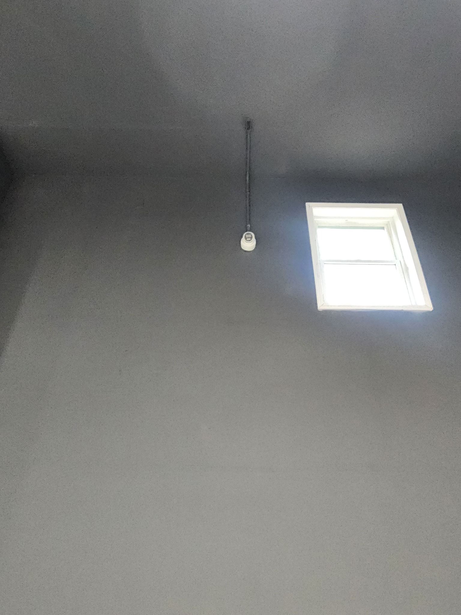 Gray room with a small window and a hanging light fixture.