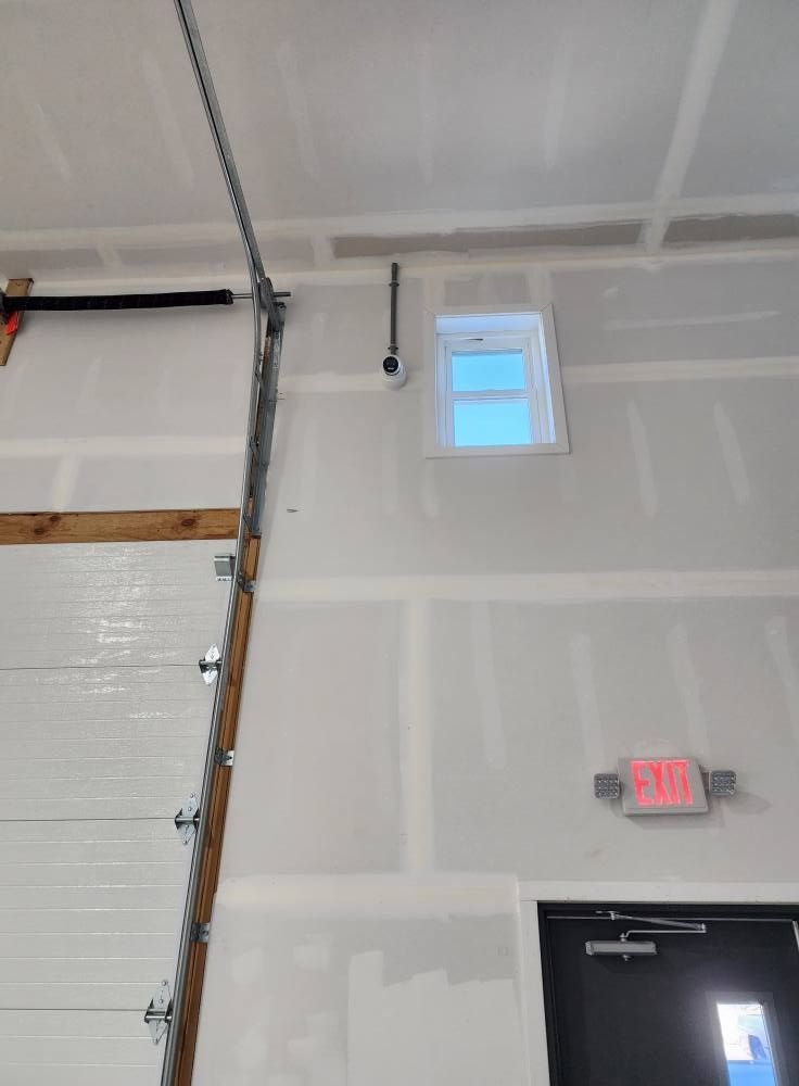 Interior view of a construction site with a garage door, small window, and an exit sign visible.