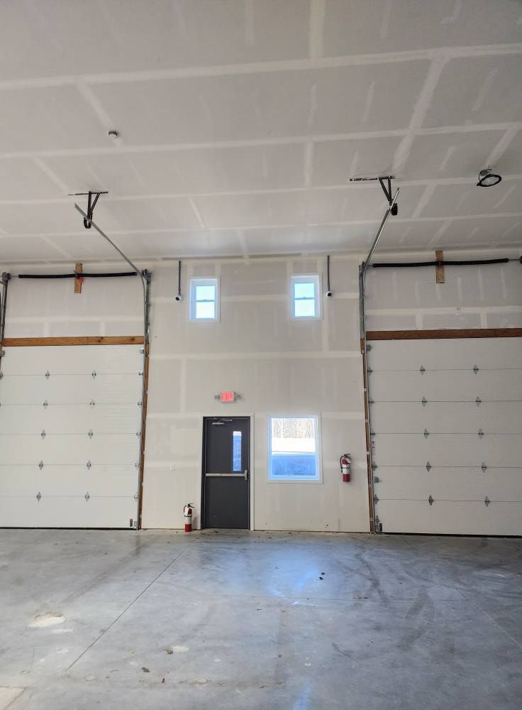 Interior view of a bare commercial space with two garage doors, a door, windows, and fire extinguisher.