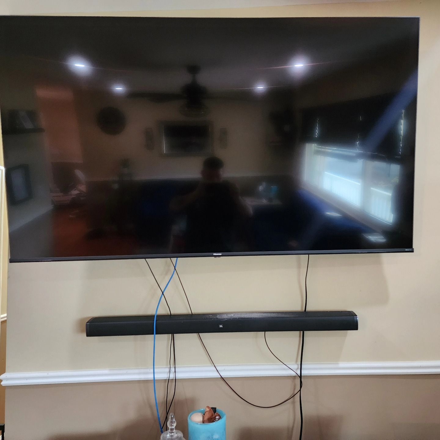 Large TV mounted above a soundbar on a beige wall, with visible wires.