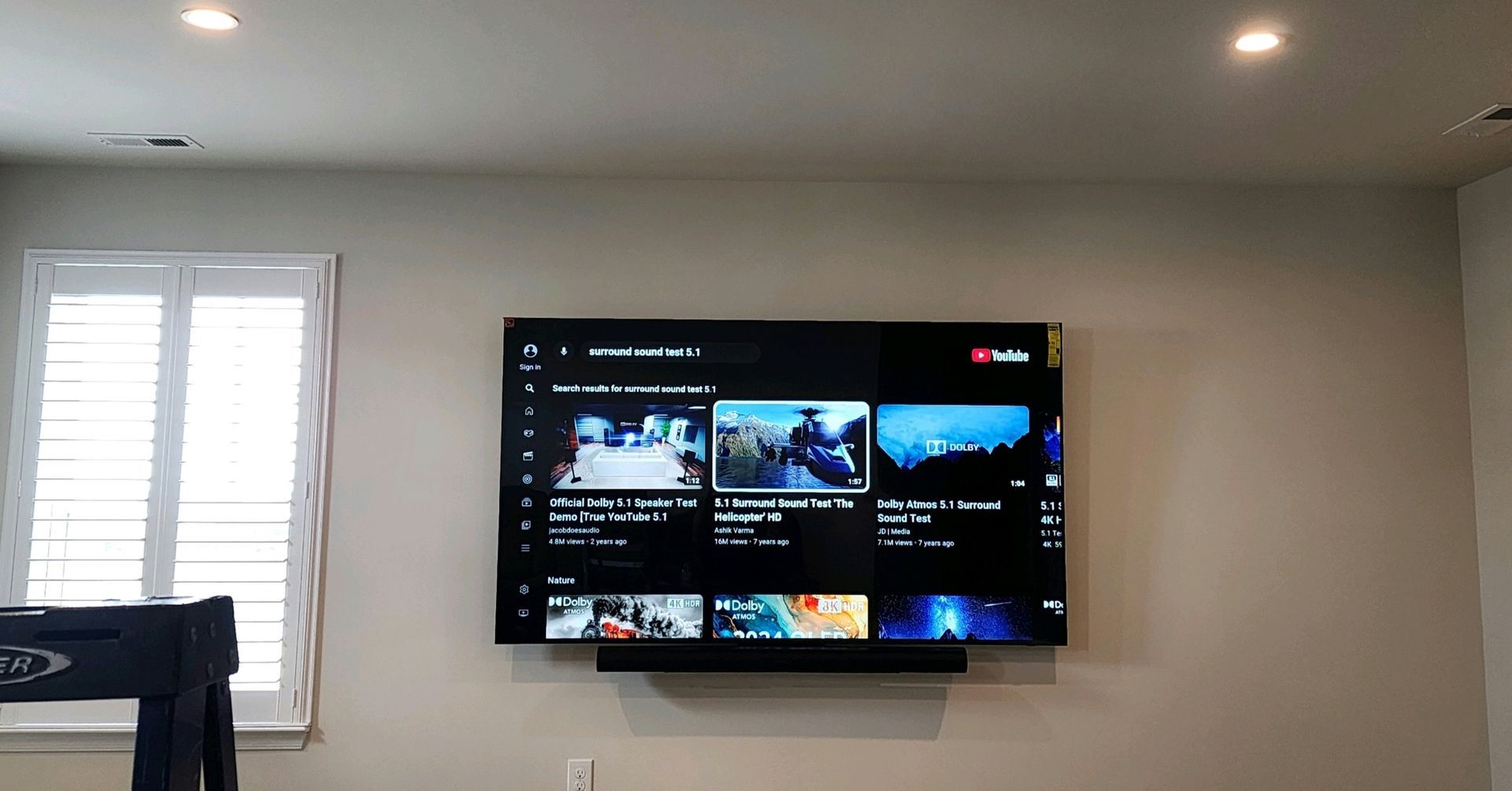 A large TV mounted on a wall displays a YouTube interface. A soundbar is below the TV.