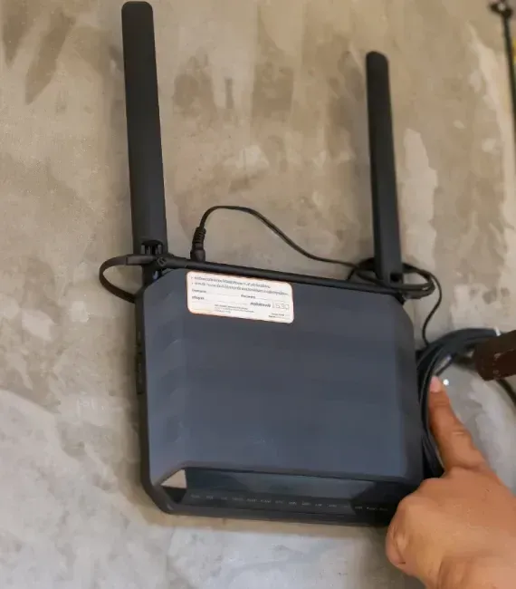 Wi-Fi router mounted on a gray wall, two antennas, hand touching the device.