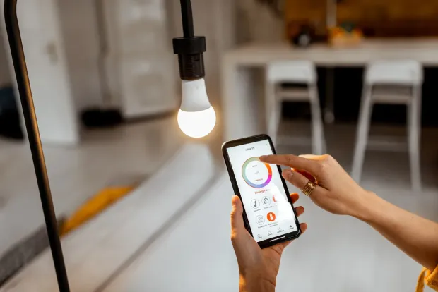 Smart home control panel on a textured wall, with an interior living room in the background.