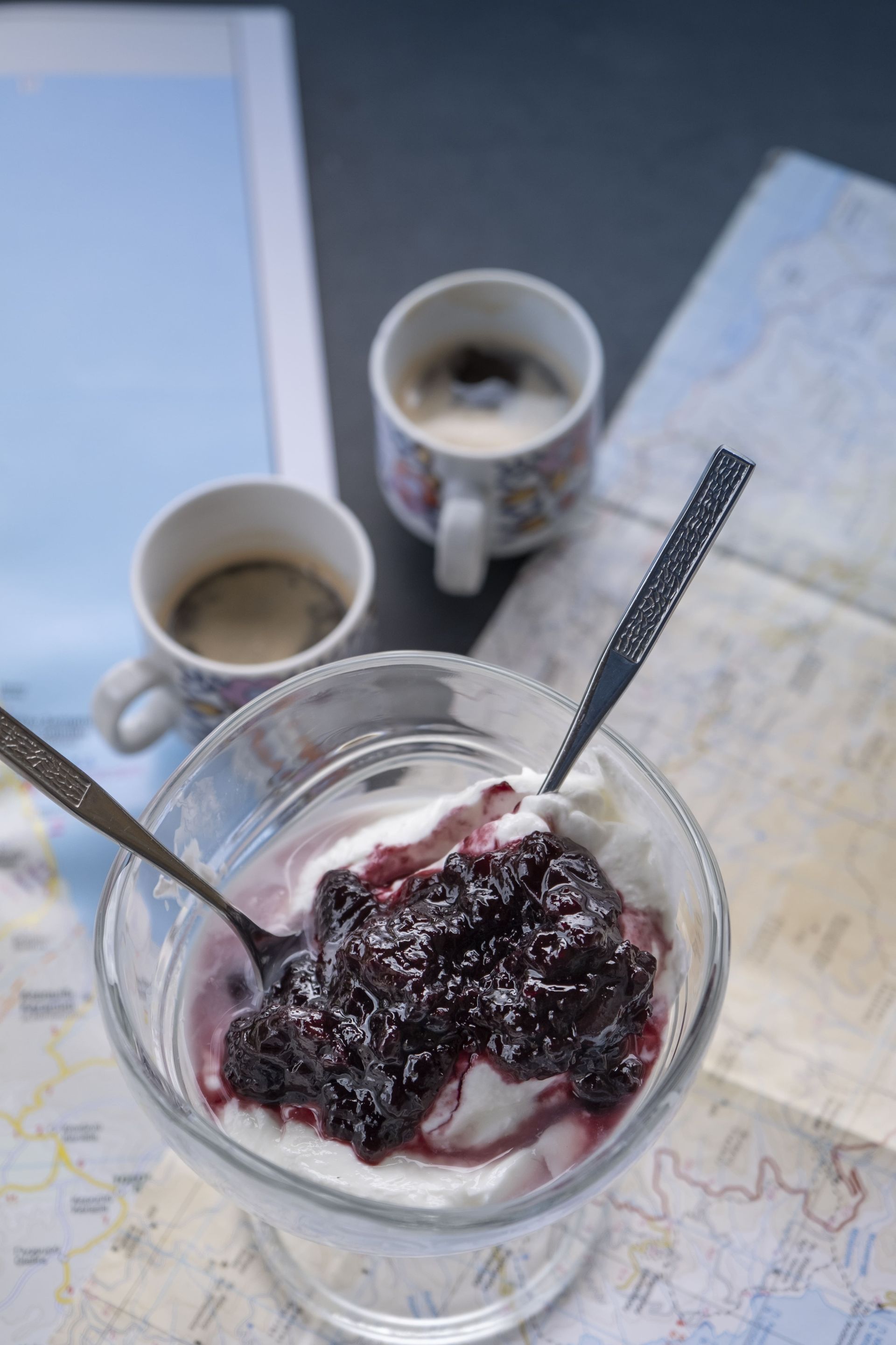 Glass of dessert with blueberry compote, coffee cups, and maps.
