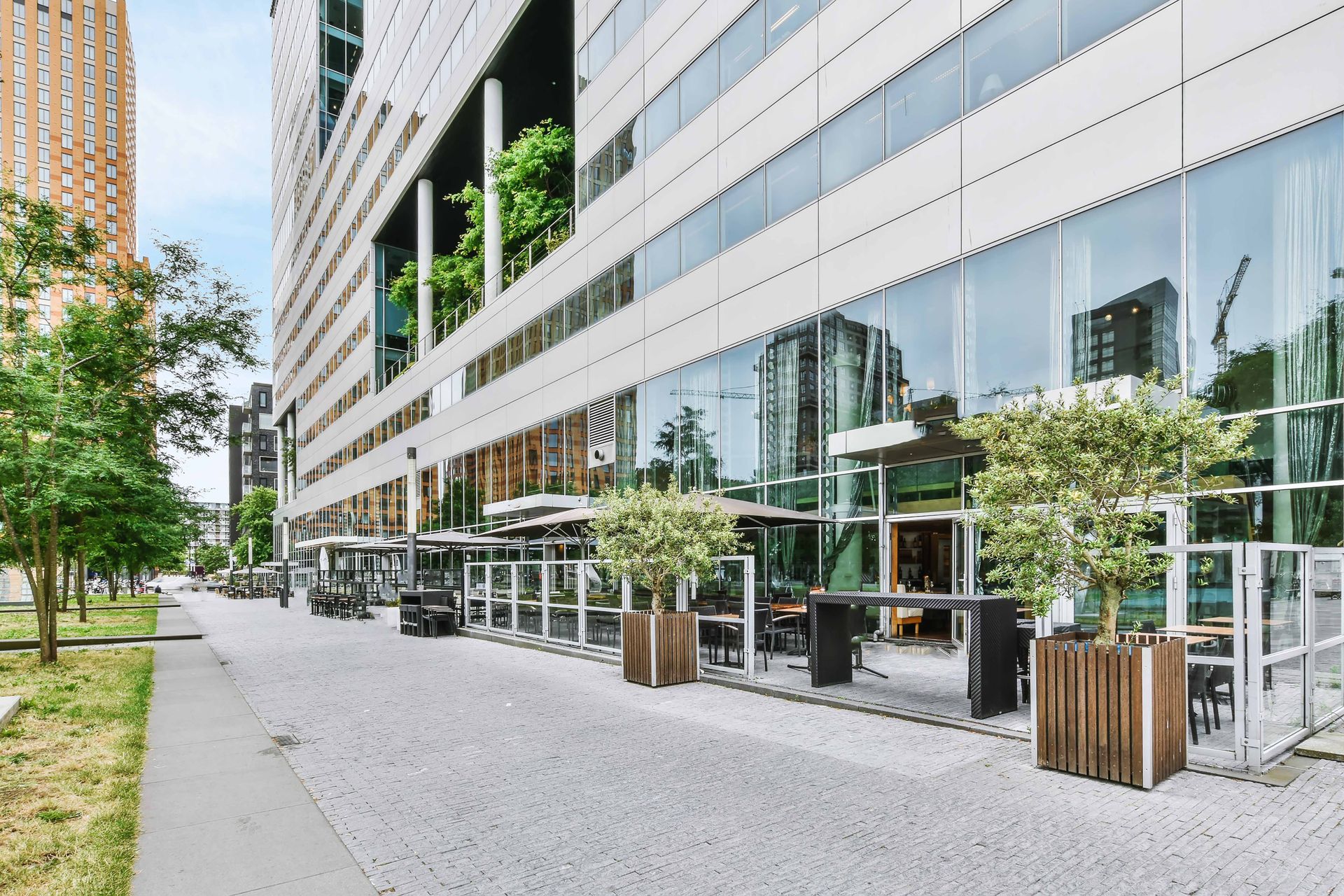 Sidewalk cafe in front of modern office building with potted trees and tables.
