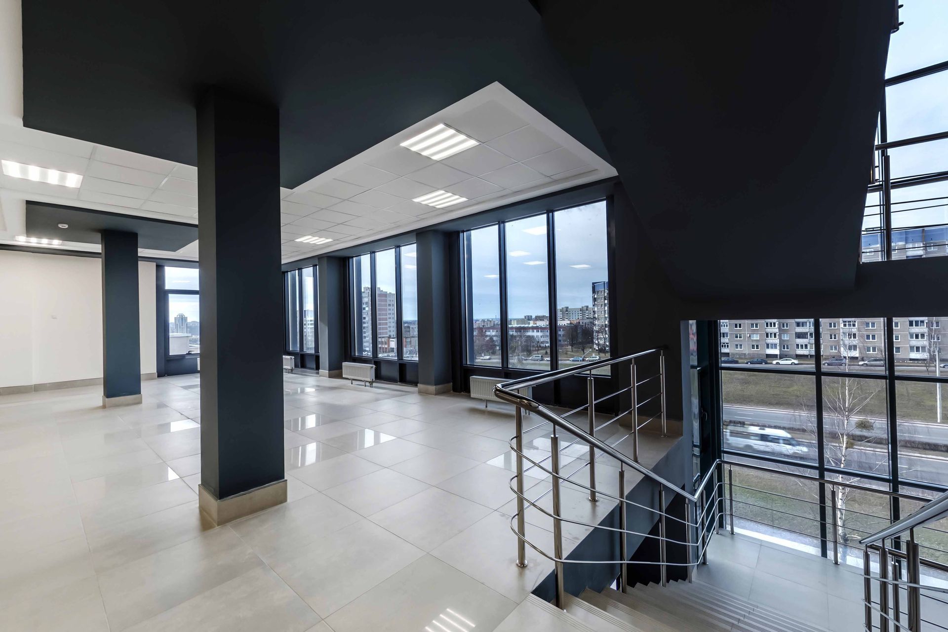 Interior of a modern building with large windows, columns, and a staircase, showcasing a spacious, empty area.