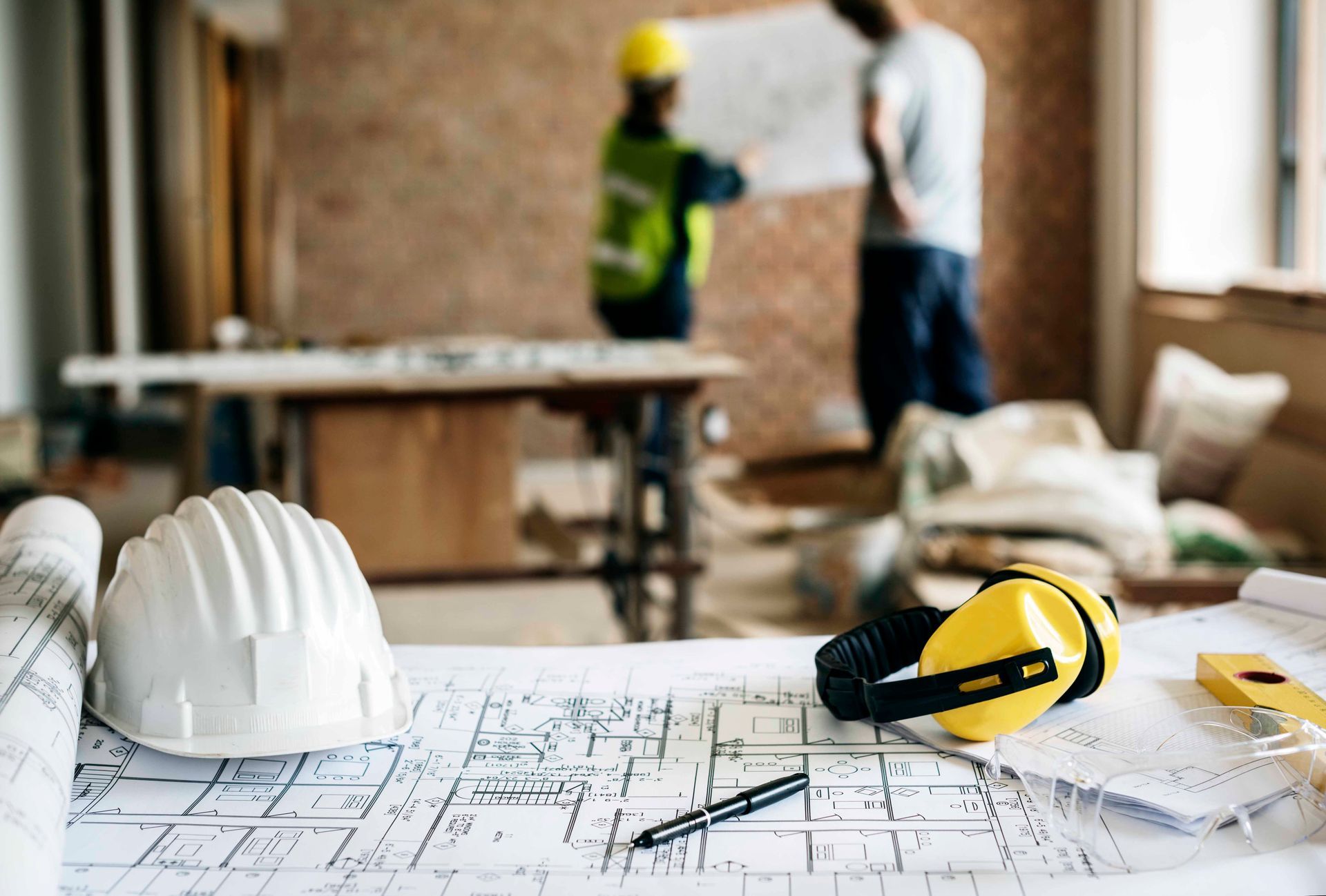 Hard hat, blueprints, and ear protection on table.