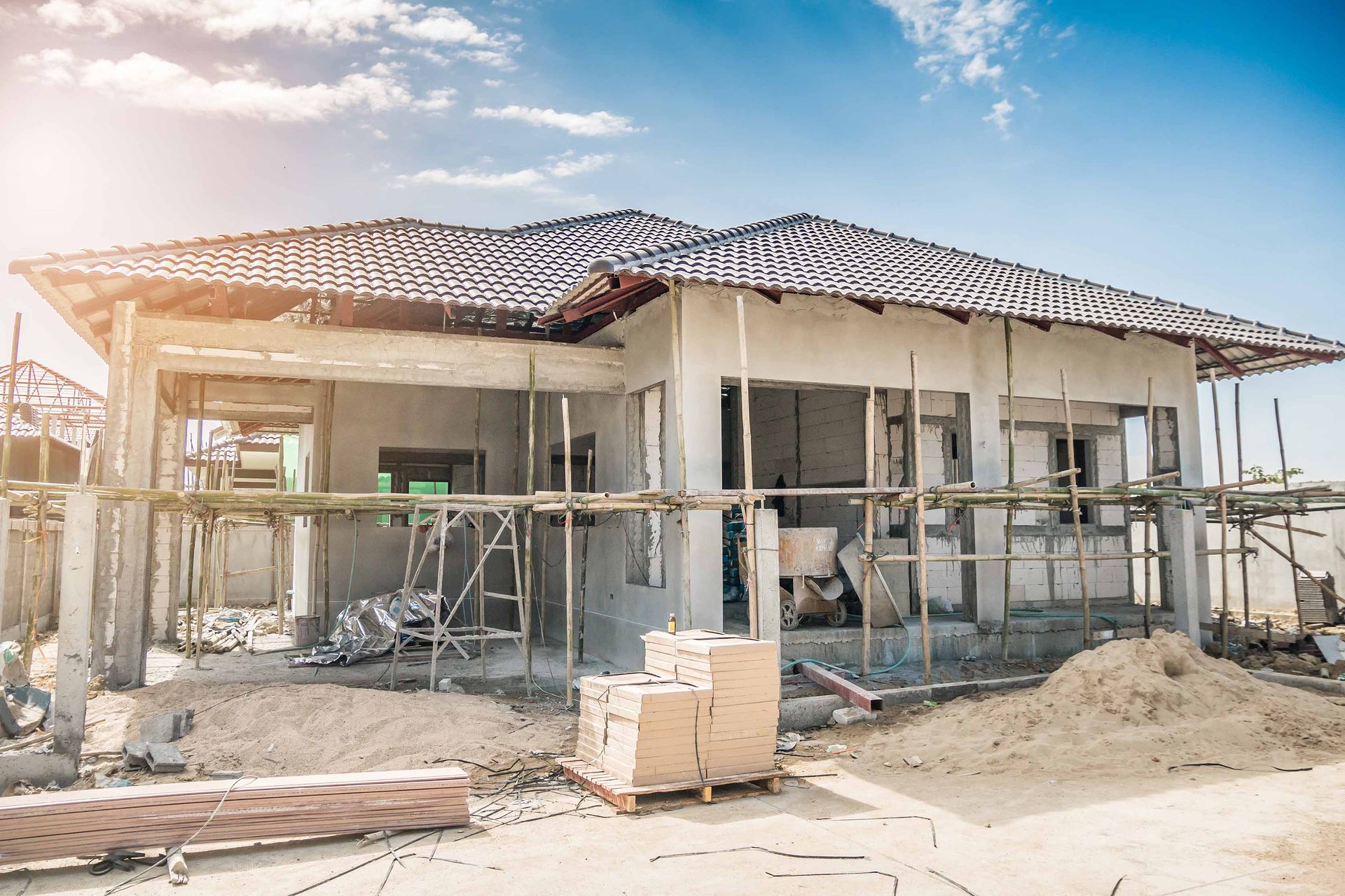 Construction of a one-story house. Partially built, with scaffolding, wood, and concrete visible.