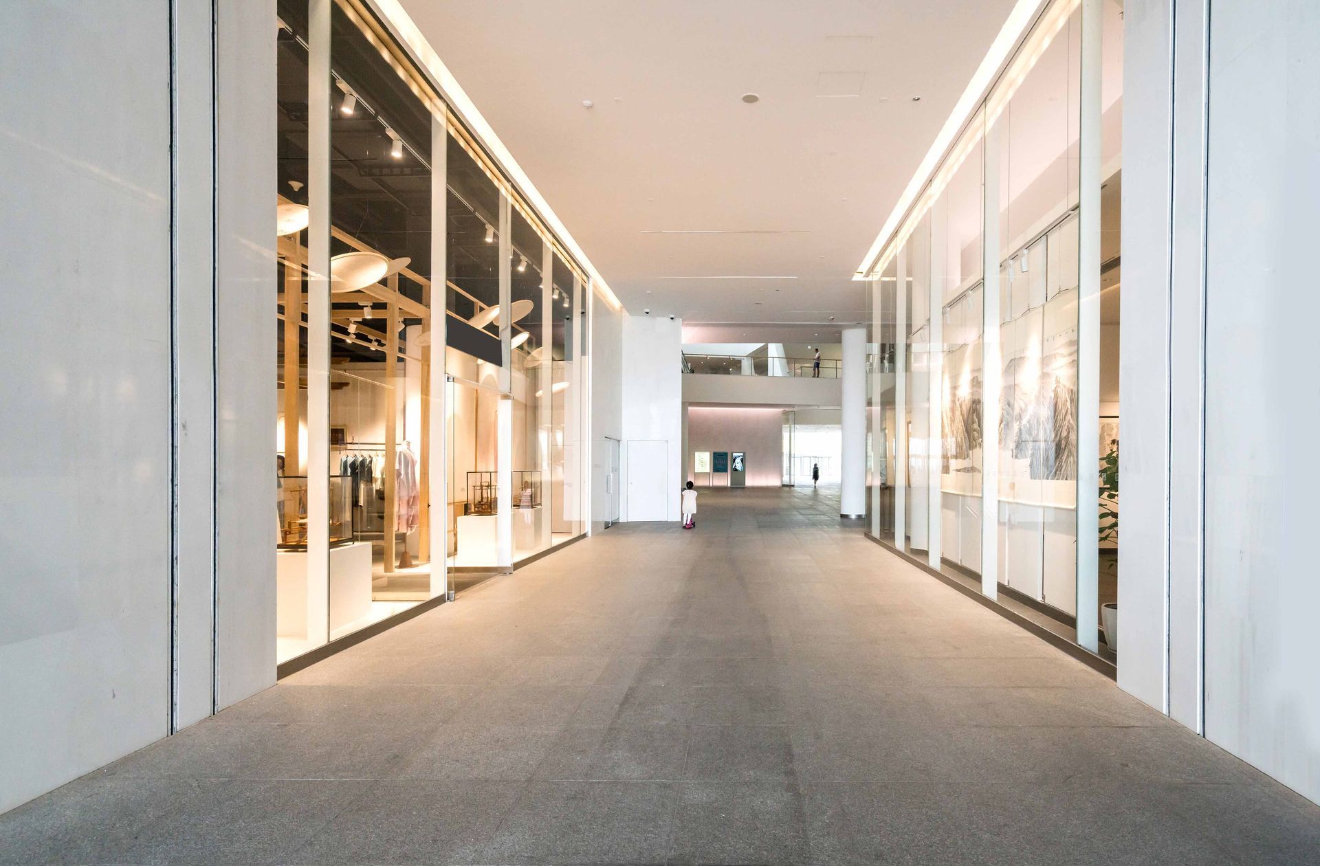 Long hallway in a modern building with displays on the left and right, and bright lighting.