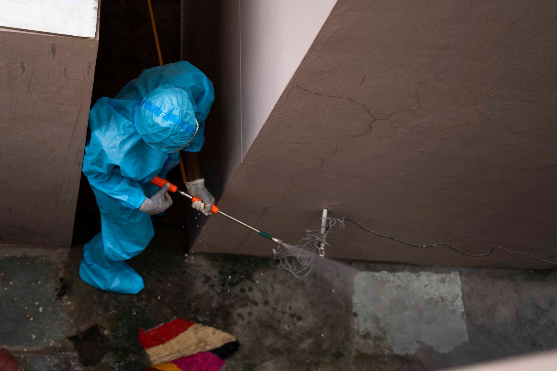 Person in blue hazmat suit sprays disinfectant in a doorway.
