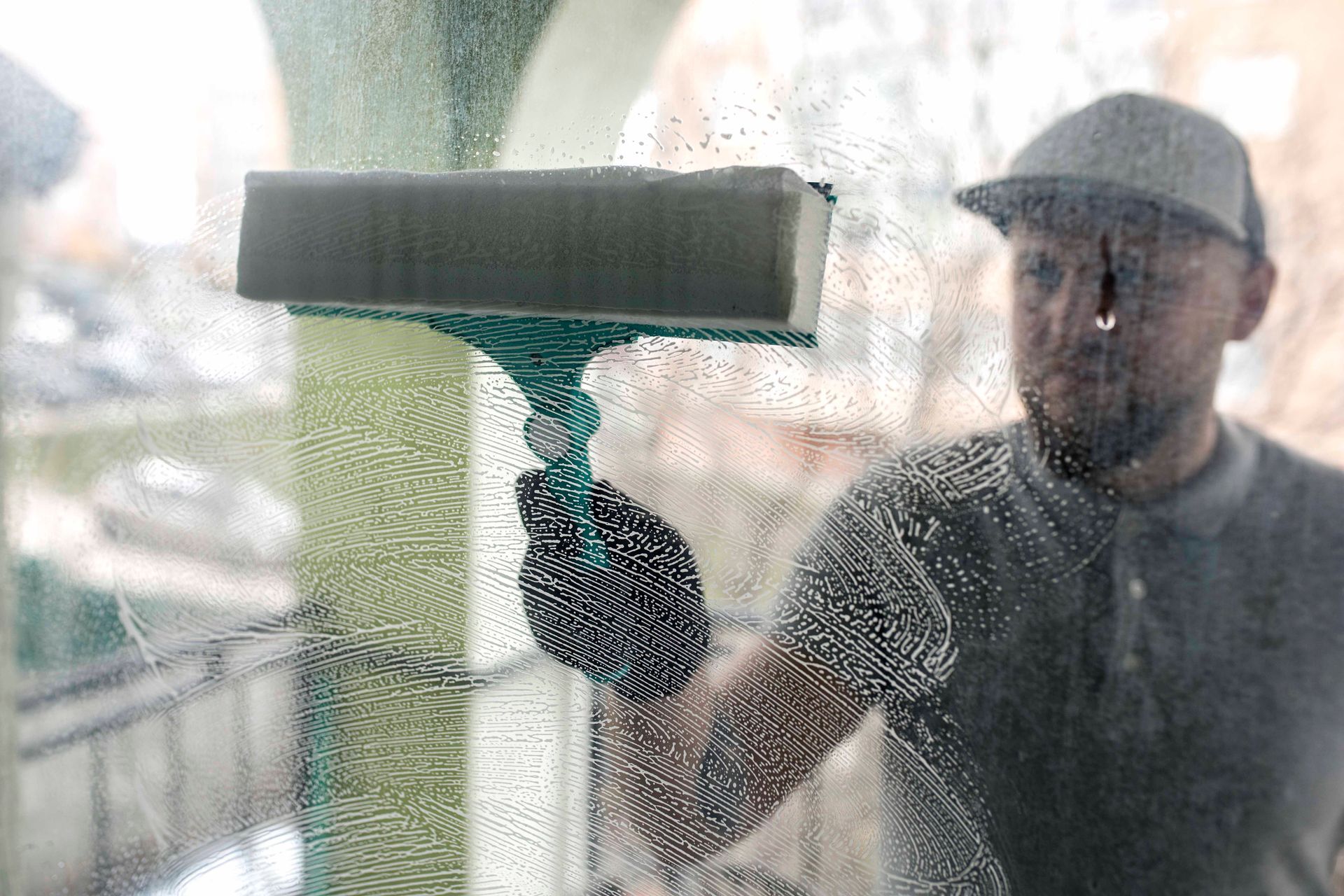 Person cleaning a window with a squeegee; soapy, blurred glass.