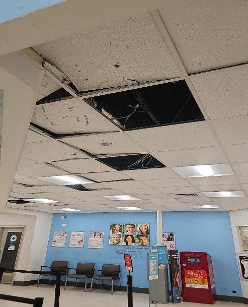 Damaged ceiling tiles in a waiting area; several panels are missing, revealing dark interior.