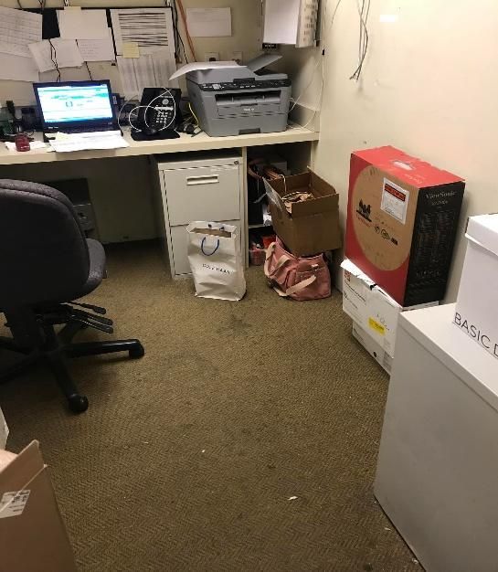 Office space with cluttered desk, printer, boxes, and file cabinets.