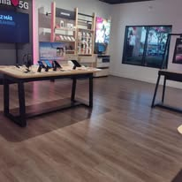 Interior of a T-Mobile store with display tables and product displays, with a large window and wood-look flooring.