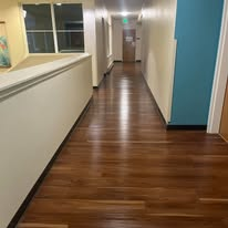 Long, wooden hallway with a bright window at the end, and a blue door on the right.