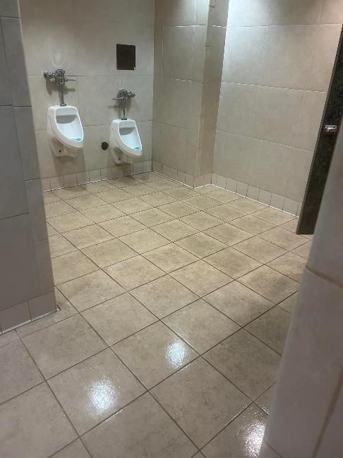 Public restroom with two urinals, light-colored tiles, and walls.