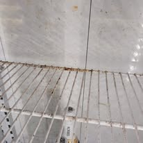 Wire shelf with rust and debris against a tiled surface.