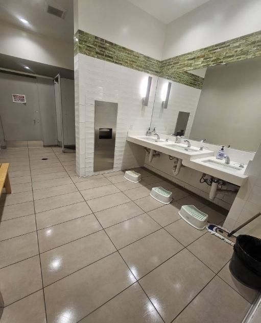 Public restroom with sinks, mirrors, stalls, and step stools on a tiled floor.