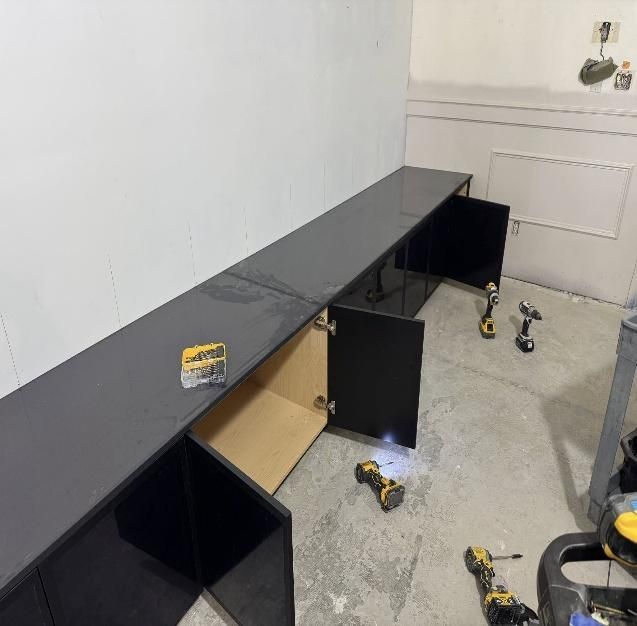 Black cabinets being installed against a white wall.