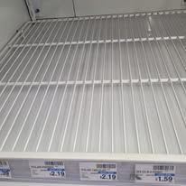 Empty white wire shelf in a store, with price tags below.