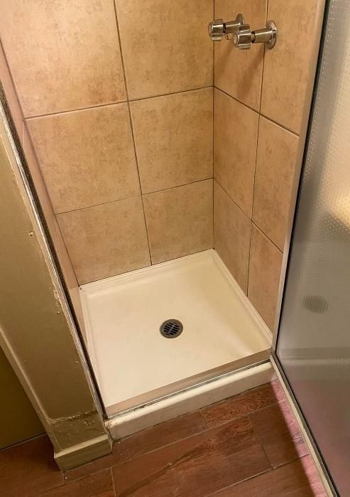 Shower stall with beige tile walls and white base, chrome shower head, and glass door.