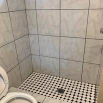 Tiled shower with black and white floor, and a toilet in the foreground.
